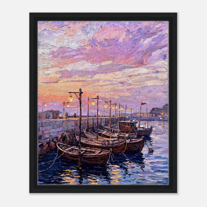 A framed canvas art print depicting a colorful sunset harbor scene with wooden boats moored in calm water under a pink, purple, and orange sky.