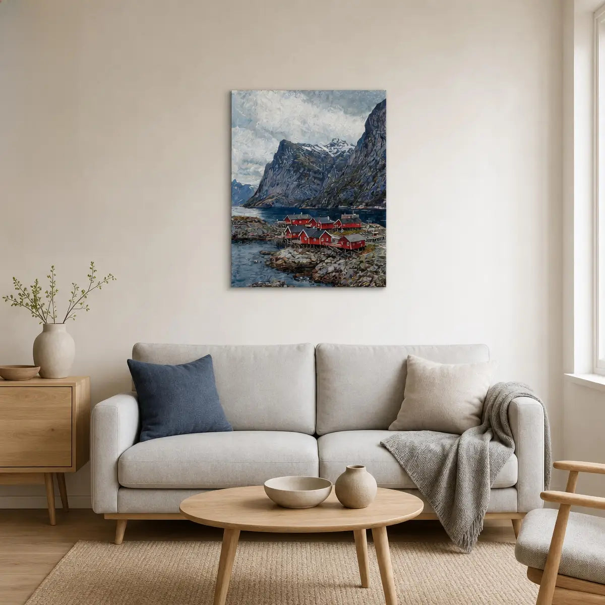 A vertical canvas print of a dramatic mountain fjord with red canoes, displayed on a beige wall above a modern light gray sofa in a minimalist living room.