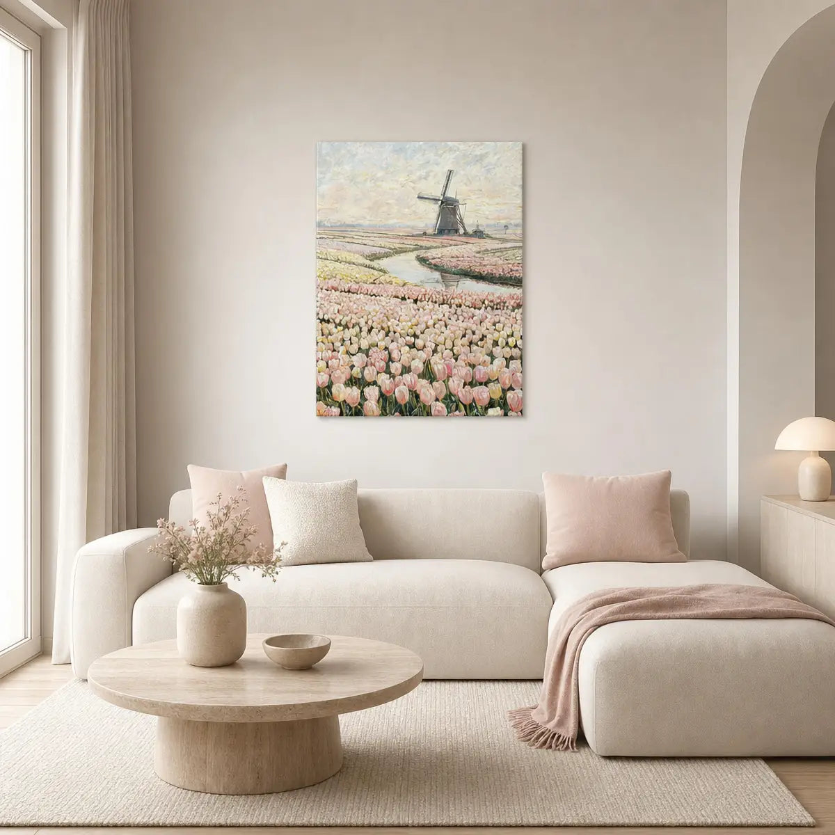 A framed canvas print of a Dutch tulip field with a windmill hangs on a beige wall above a cream-colored sectional sofa in a styled living room.