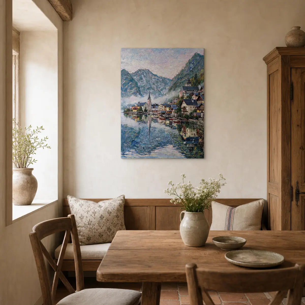 A framed impressionist landscape painting of a mountain village by Lake Balaton is displayed on a beige wall in a rustic dining room setting with a wooden table, chairs, and potted plants.