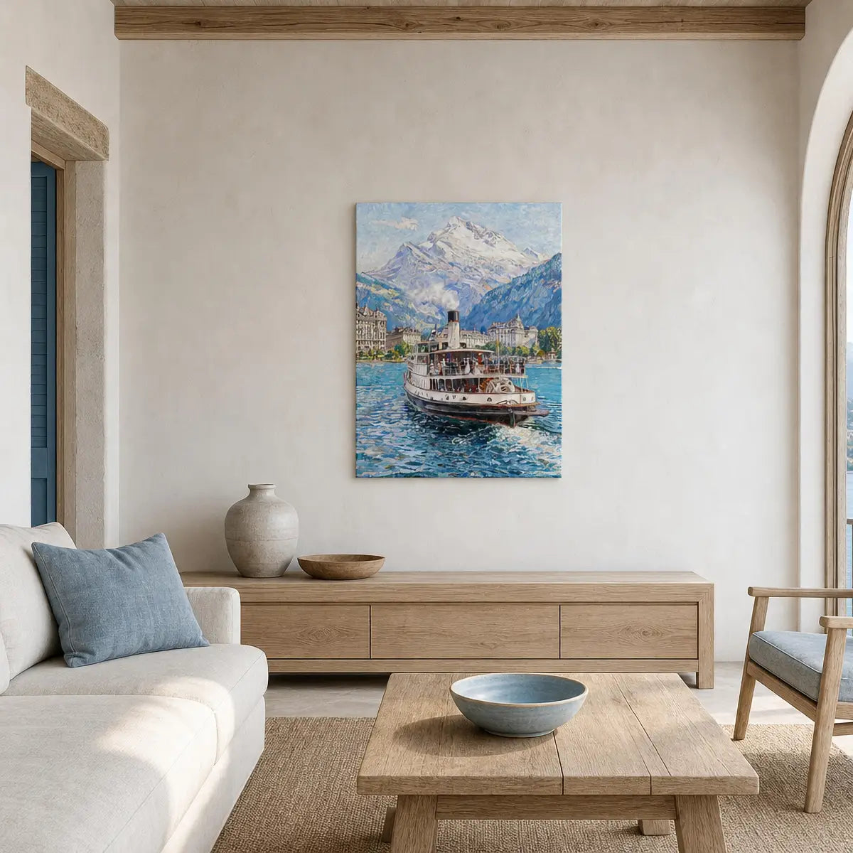 A framed-style wall art print depicting a lake scene with a boat and snow-capped mountains, displayed above a light wood console in a bright, modern living room with a sofa, coffee table, and vase.