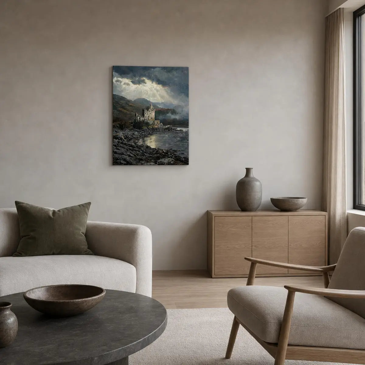 A vertical canvas print of a dramatic coastal landscape with a castle, displayed on a beige wall in a modern, minimalist living room with a sofa, armchair, and wooden cabinet.