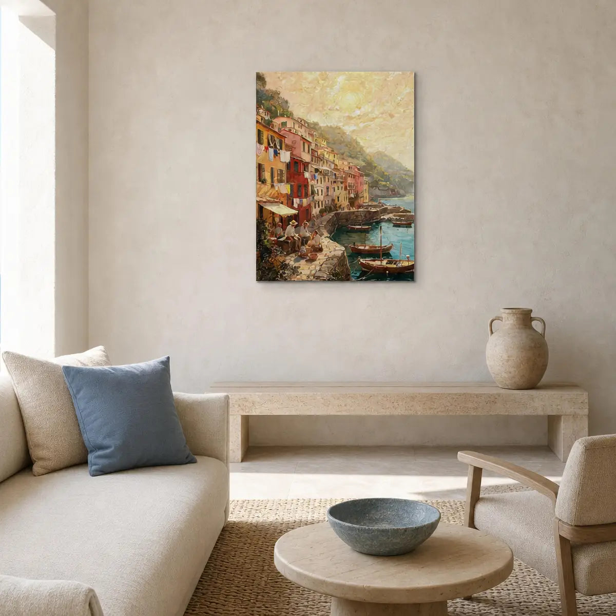 A vertical canvas print of a colorful coastal village harbor painting, styled on a textured beige wall in a modern living room setting above a low wooden bench and sofa.