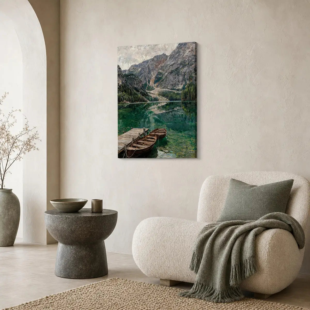 A vertical canvas wall art print depicting a scenic mountain lake with wooden boats, styled in a modern, neutral-toned living room next to a cream-colored armchair and a gray throw blanket.