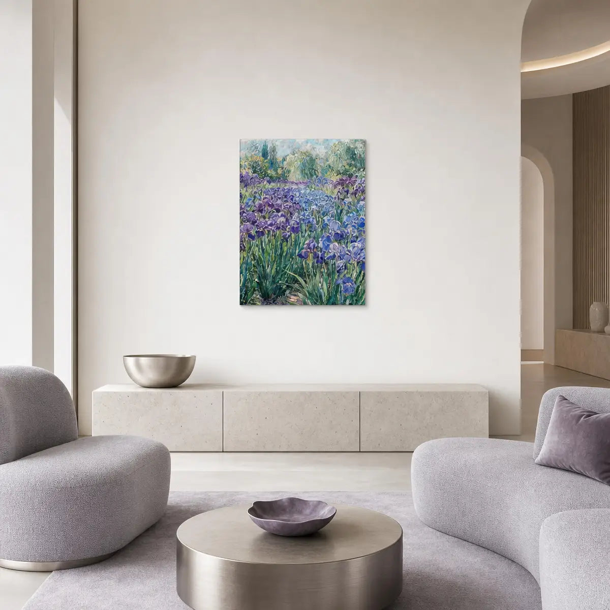 A square canvas art print depicting a vibrant purple and blue iris field hangs on a neutral beige wall in a modern, minimalist living room with gray sofas and a round metallic coffee table.