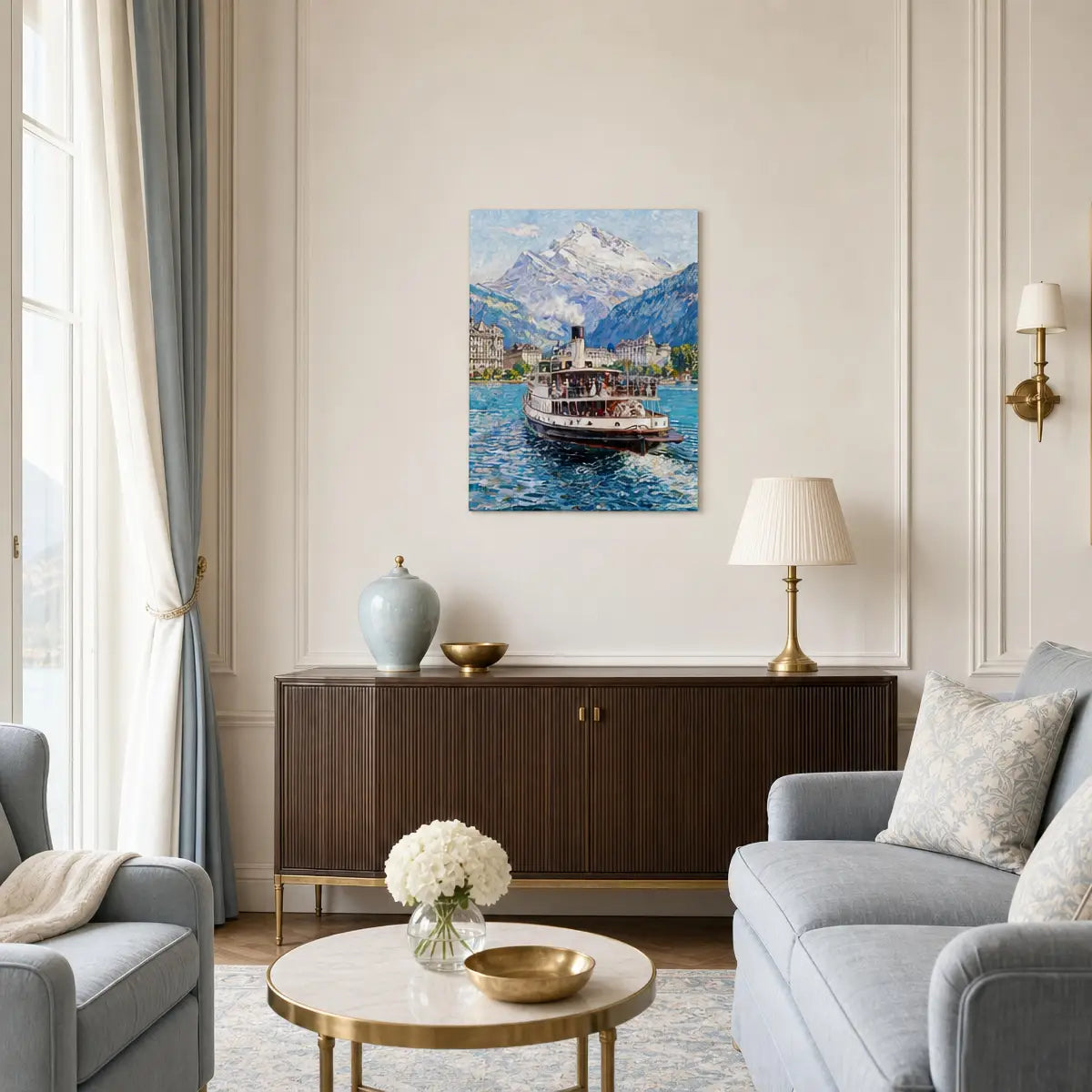 A framed canvas print of a scenic mountain lake with a paddle steamer boat, displayed on a cream wall in a styled living room with a wooden sideboard, lamps, and gray sofas.
